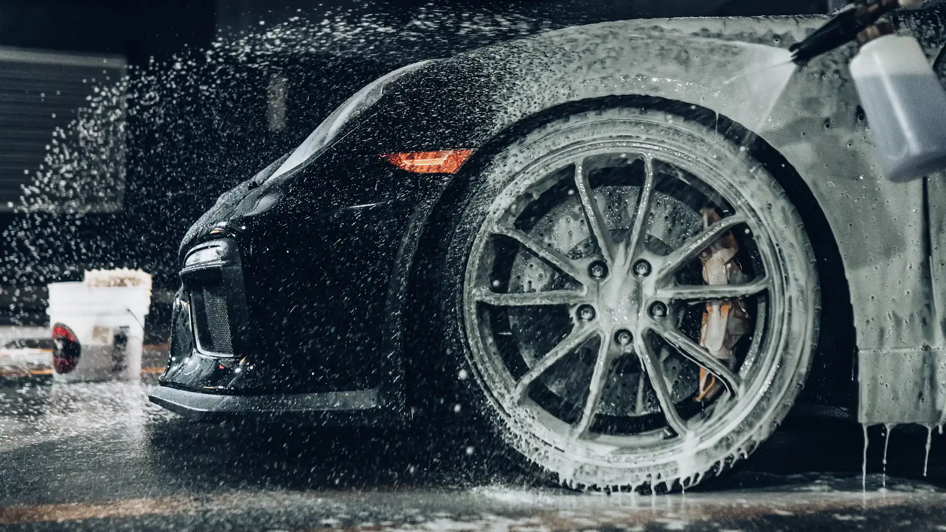 Carro deportivo negro cubierto de espuma durante un detailing profesional